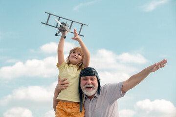 Grandson child and grandfather playing with toy plane against summer sky background. Generations ages.