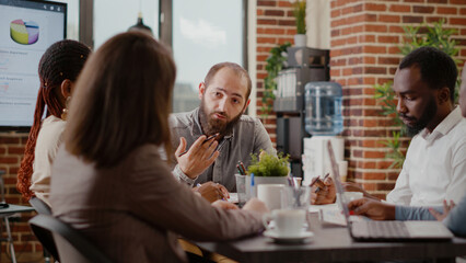 Close up of employee meeting with coworkers for project planning in office. Man talking to workmates to design marketing strategy, brainstorming ideas and using documents with statistics.