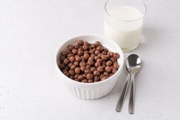 White bowl with chocolate cereal on white table. Served with milk, and spoons. Breakfast and start of the day