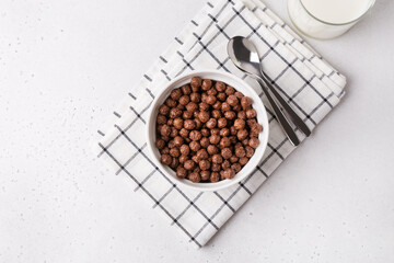 White bowl with chocolate cereal on white table. Served with milk, and spoons. Breakfast and start...