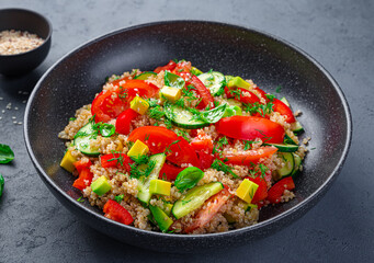 Tabbouleh salad with quinoa, tomatoes, cucumber, avocado and red pepper on a gray-blue background.