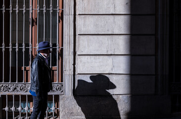 Adult man in hat and jacket walking on street with sunlight and shadow. Madrid, Spain
