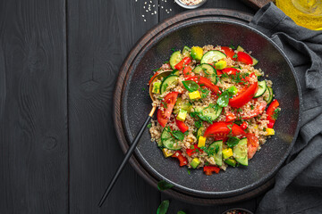 Healthy salad with quinoa, vegetables and fresh herbs on a black background.