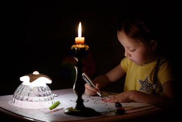 Little girl draws fantasy characters near candle in a dark room. Child doing favorite thing during...