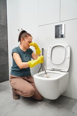 woman covering nose to avoid bad smell while cleaning a smelly toilet bowl