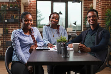 Happy african american business company team sitting at desk in modern office interior. Marketing agency professional colleagues sitting at table while smiling and looking at camera.