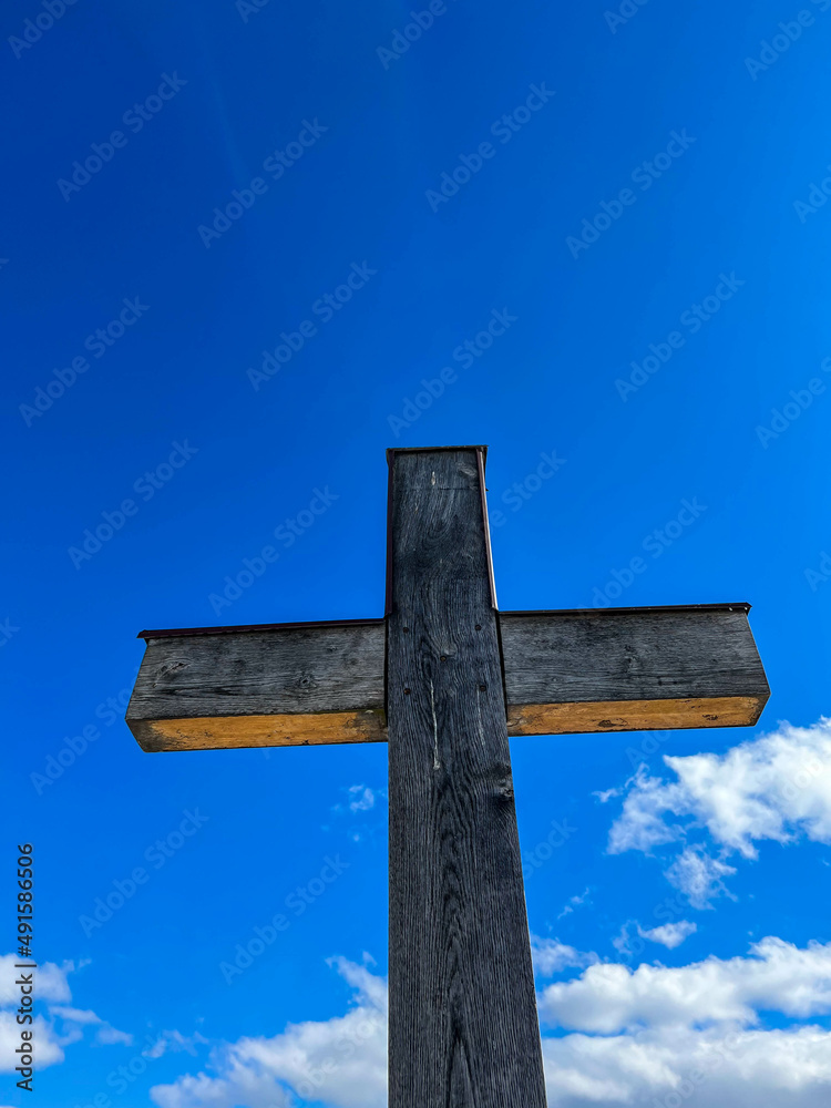 Wall mural Simple oak wood catholic cross against deep blue sky with white clouds vertical image.