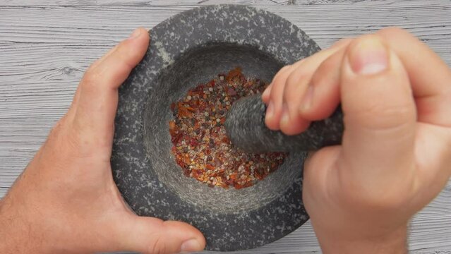 Top view of the hand with heavy pestle grinding mix of spices and peppers