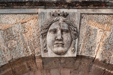 A stone face above the arch. The expression of the face above the gate. An ancient fresco.