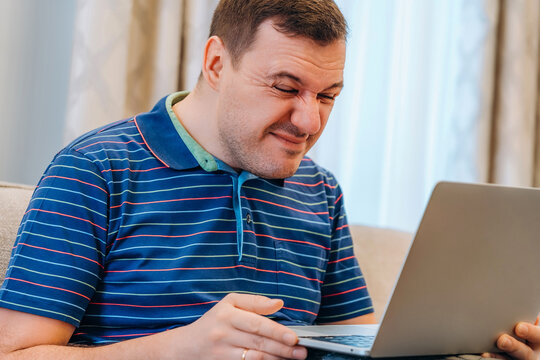 Man Squints And Tries See Something Small Or Reading Suspicious Message On Laptop Screen In Living Room At Home. Confused Millennial Man Reading News On Laptop With Cringe, Unpleasant Negative Emotion