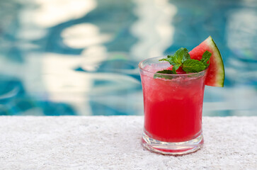 A glass of watermelon smoothie puts beside swimming pool for summer drink concept.