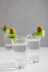 Vodka or gin clear distilled alcoholic beverage or short drink served in three shot glasses garnished with slice of  fresh raw cucumber and pickled or marinated olives on white wooden table at kitchen