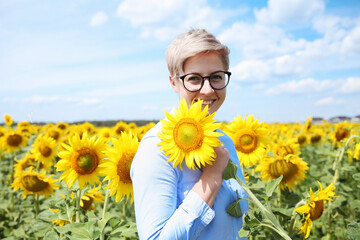 Young beautiful blonde woman standing in sunflower field.
 