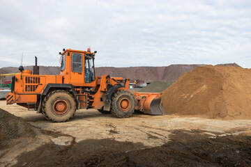 The front loader picks up gravel or crushed stone in the front bucket. Heavy construction machinery at the construction site. Transportation of materials at a concrete plant.