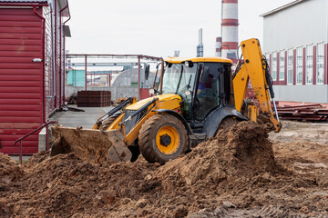 The excavator backfills the pit with the front bucket. Moves soil around the construction site. Close-up. Heavy construction equipment.