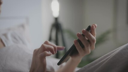Unrecognizable woman uses smartphone while lying in bedroom. Hands and phone close up. - Powered by Adobe