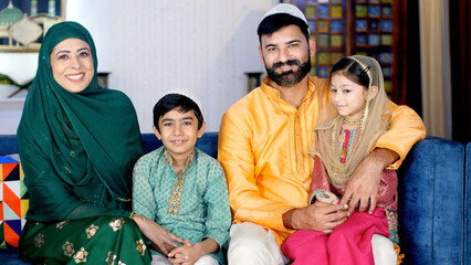 Modern nuclear Muslim family in India - Happy family with two kids and young parents. A happy Muslim family in an ethnic dress sitting together in the living room while posing for the camera - family