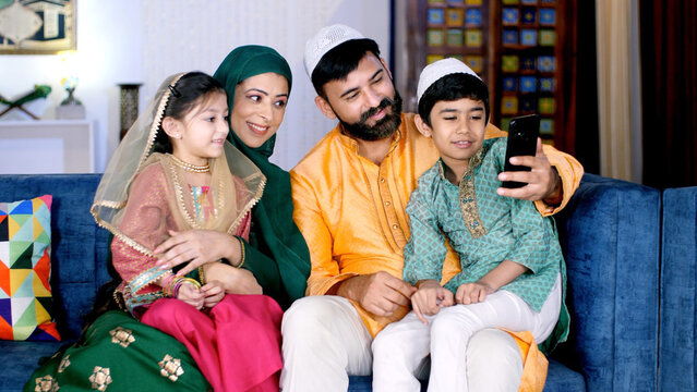 A joyful Muslim family making a video call on their smartphone together at home. A cheerful Indian family using a mobile together while sitting together in the living room - leisure time, an electroni - Powered by Adobe