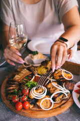 Plate with shashlyk and meat delicacies. Barbecue, baked potatoes with lard and onions. Girl's hand holds a glass of wine
