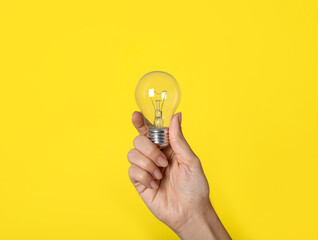 Woman holding incandescent light bulb on yellow background, closeup