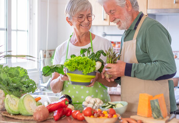 Attractive senior couple preparing vegetables together in the home kitchen. Caucasian elderly people enjoying healthy eating - Powered by Adobe