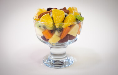 Fototapeta na wymiar Close up on a glass bowl filled with a fresh and colorful fruit salad. Orange fruit, kiwi, papaya, melon, apple, almond