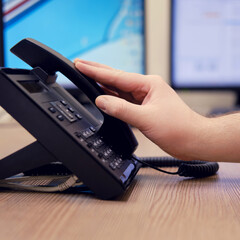 A man hand puts a telephone receiver at the monitors of office computers. Ending a telephone...