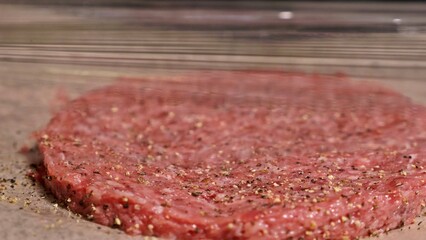 Cook makes meat medallions for burgers. Chef in black food gloves makes cutlet. Cutlets are leveled in steel ring in an even medallion. On top of pouring spices pepper and salt.