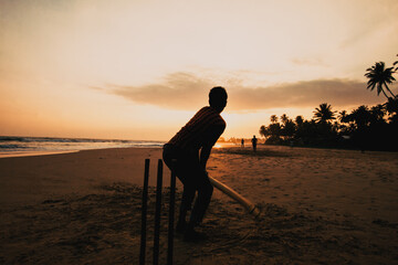 boy playing cricket at sunset on tropical beach in Sri Lanka