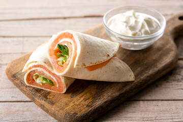 Salmon wrap sandwich roll with cheese and vegetables on wooden table