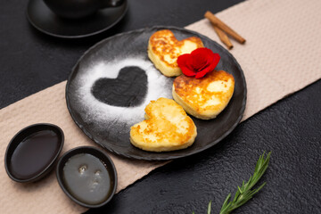 Curd cheesecakes (pancakes) in the shape of a heart with honey and jam on a black plate