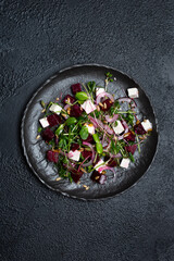 Salad of microgrin, beetroot and cheese with fresh onions and seeds on a plate on a black background. top view
