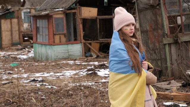a girl wearing in the Ukrainian flag looks at the destroyed houses. War in Ukraine