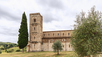 Fototapeta na wymiar Stunning architectural tandem of Belltower of Abbey Sant Antimo and tall slender cypress. Val d’Orcia, Italy