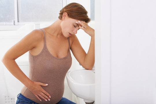 The Aches And Pains Of Pregnancy. A Pregnant Woman Struggling With Morning Sickness In The Bathroom.