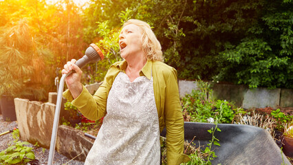 Alte Frau singt beim Blumen gießen als Lebensfreude Konzept