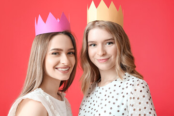 Portrait of young sisters with paper crowns on color background