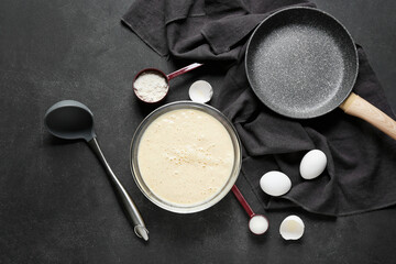 Raw batter with ladle and frying pan on dark background