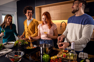 Group of friends preparing vegetarian meal in a kitchen at home.