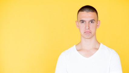 Disappointment regret. Unhappy man. Displeased situation. Upset sorrowful guy in white t-hirt with low edges of lips isolated yellow copy space.