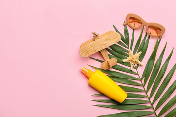 Composition with stylish sunglasses, wooden plane, bottle of sunscreen and palm leaf on pink background