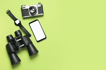 Mobile phone, binoculars, smart watch and photo camera on green background