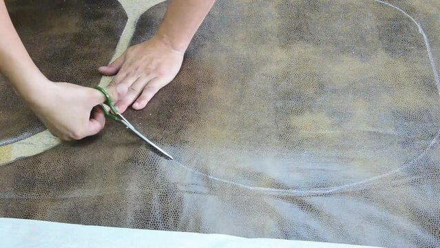 The craftsman cuts leatherette with scissors, makes patterns for upholstered furniture, close-up.