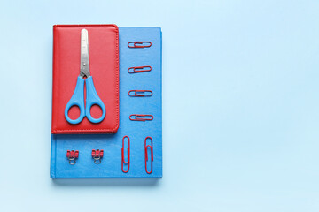 Notebooks, scissors and clips on color background