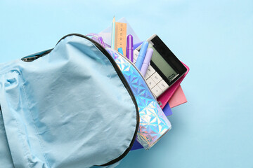 Stylish backpack with different stationery on color background, closeup