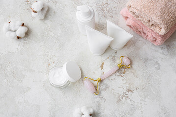 Cosmetics, facial massage tool and cotton flowers on light background
