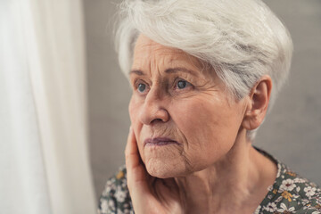 Old caucasian sad lady looking through the window with a melancholic gaze. High quality photo