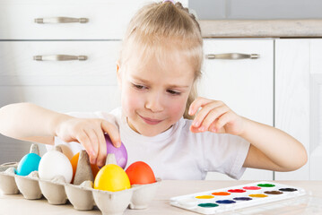 Cute girl with Easter eggs at the table in the kitchen.
