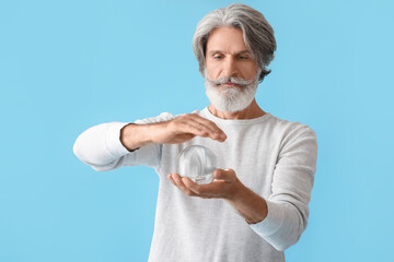 Mature man with crystal ball on color background