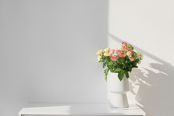 White vase with beautiful roses on shelf near light wall